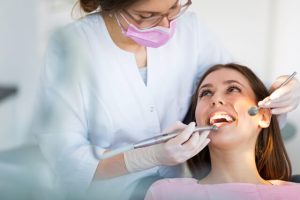 The patient listens to her dentist while the dentist cleans her teeth.